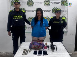 En la imagen se ve una mujer detenida bajo custodia de integrantes de la Policía Nacional. Detrás suyo, un backing institucional.