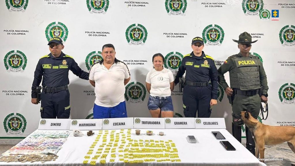 en la imagen se ven dos personas detenidas bajo custodia de la Policía Nacional. Frente a ellos una mesa con elementos incautados. Detrás un backing institucional.