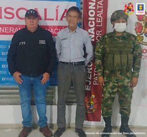 en la imagen se ve una persona detenida bajo custodia del CTI y el Ejército. Detrás suyo un backings institucionales. 