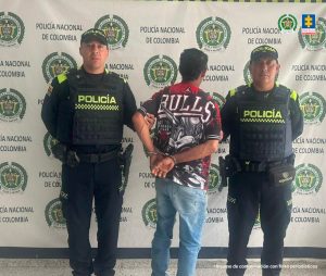 En la imagen un hombre de espaldas, esposado y custodiado por dos funcionarios de la Policía Nacional.