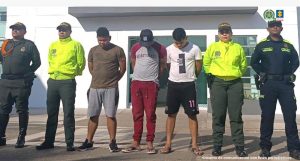 Estas tres personas, aparecen custodiadas por unidades de la Policía Nacional, detrás hay un pendón institucional y están esposados con sus manos al frente.