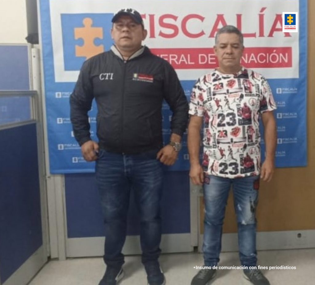 en la imagen se ve una persona detenida en custodia de un investigador del CTI. Detrás suyo un backing de la Fiscalía.