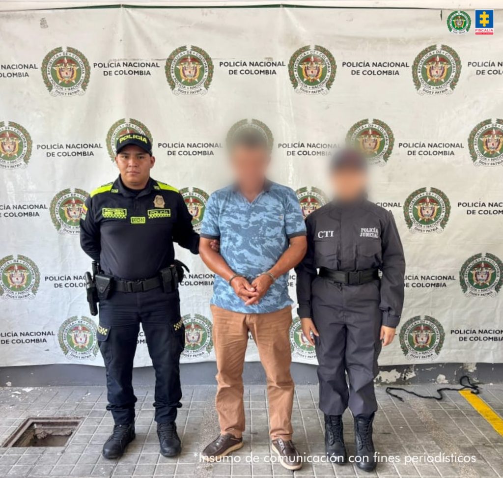 en la imagen se ve un hombre detenido bajo custodia de un investigador del CTI y un uniformado de la Policía Nacional. Detrás un backing institucional.