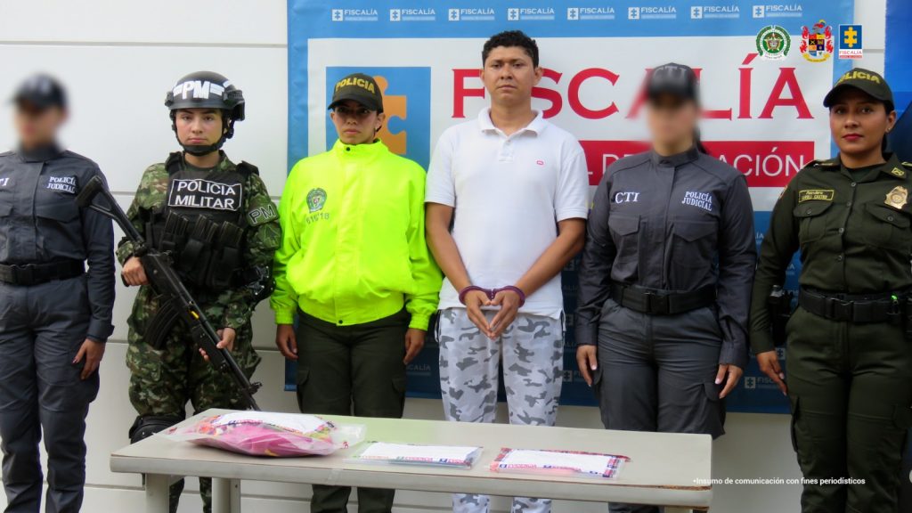 En la imagen se ve una persona detenida bajo custodia de investigadores del CTI, Policía y Ejército. Detrás suyo, backings institucionales.