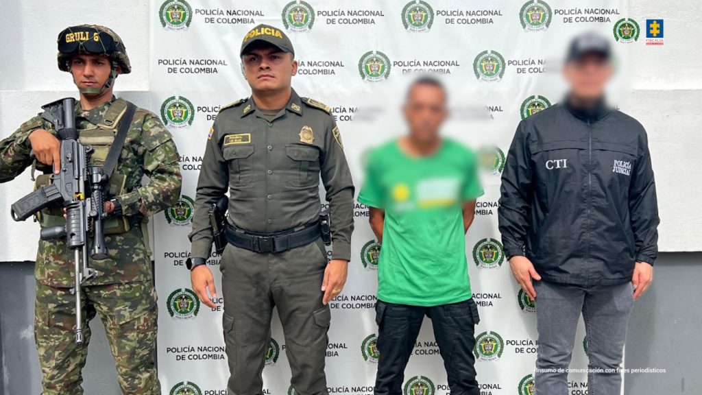 en la imagen se ve una persona detenida bajo custodia de un investigador del CTI, Policía y Ejército. Detrás, un backing institucional.