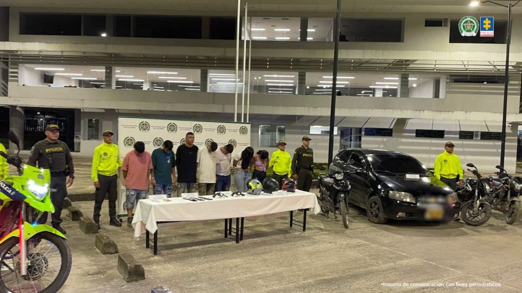 en la imagen se ven varias personas detenidas bajo custodia de uniformados de la Policía Nacional. Detrás suyo un backing institucional. Frente a ellos, una mesa con elementos incautados y a los lados un vehículo y motos incautadas.
