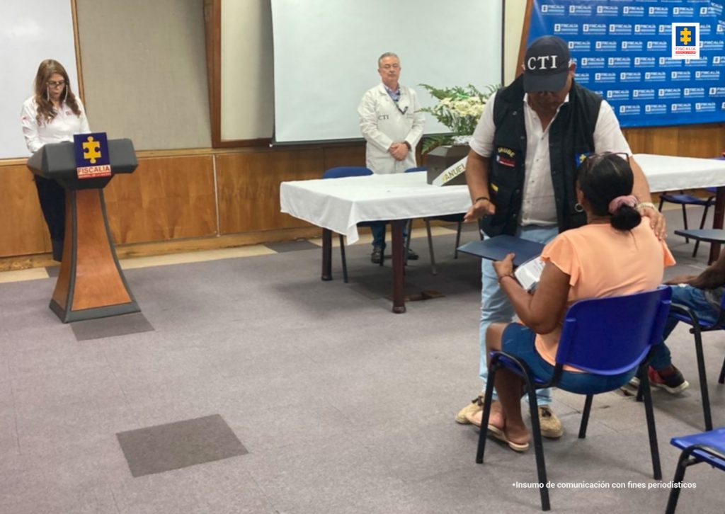 En la fotografía aparece un funcionario de la Fiscalía con ropa institucional entregando una carpeta a una señora de espalda que está vestida de camiseta naranja.