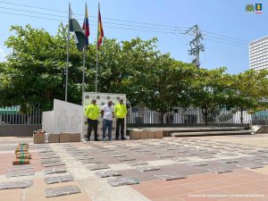 En la fotografía está un hombre moreno, calvo, de pie, con los brazos atrás, vestido de camiseta manga corta blanca, jean azul, tenis negro, acompañado por dos agentes de la Policía. Delante de ellos se ven los 58 paquetes de marihuana incautado.
