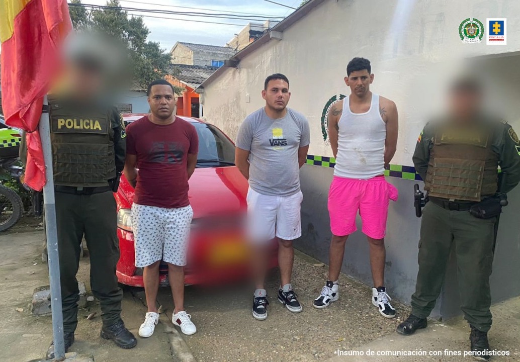 En la imagen se observan tres hombres en bermudas, tenis y camisetas custodiados por dos agentes de la Policía Nacional delante de un carro que fue in inmovilizado.