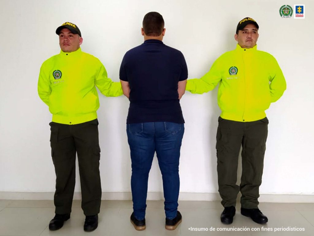 En la imagen se observa a un hombre de espalda vestido con jean y camiseta custodiado por dos agentes de la Policía Nacional.