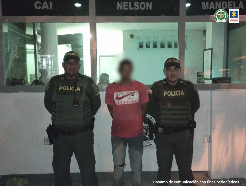 En la imagen se observa a un hombre con camiseta roja y jean, custodiado por dos policías en un CAI.