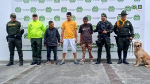 En la imagen se ven tres personas detenidas bajo custodia de integrantes de la Policía Nacional. Detrás suyo un backing institucional.