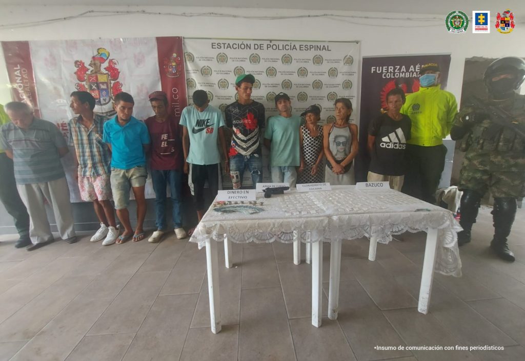 en la imagen se ven 10 personas detenidas bajo custodia de la Policía, Ejército y Fuerza Área. Detrás suyo un backing alusivo a cada una de las instituciones en mención.