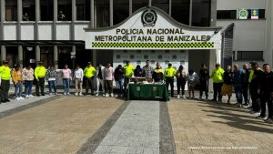 En la imagen se ve un grupo de personas detenidas bajo custodia de uniformados de la Policía Nacional. Delante suyo una mesa con elementos incautados. Detrás un backing