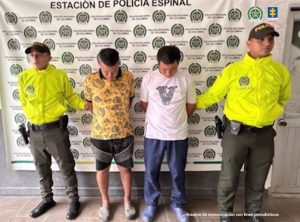 en la imagen se ven dos personas detenidas bajo custodia de integrantes de la Policía Nacional. Detrás suyo un backing institucional.