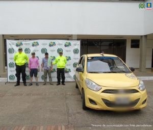 En la imagen se ven dos hombres detenidos bajo custodia de la Policía Nacional, también se ve un taxi a su lado el cual les fue inmovilizado y un backing institucional detrás suyo.