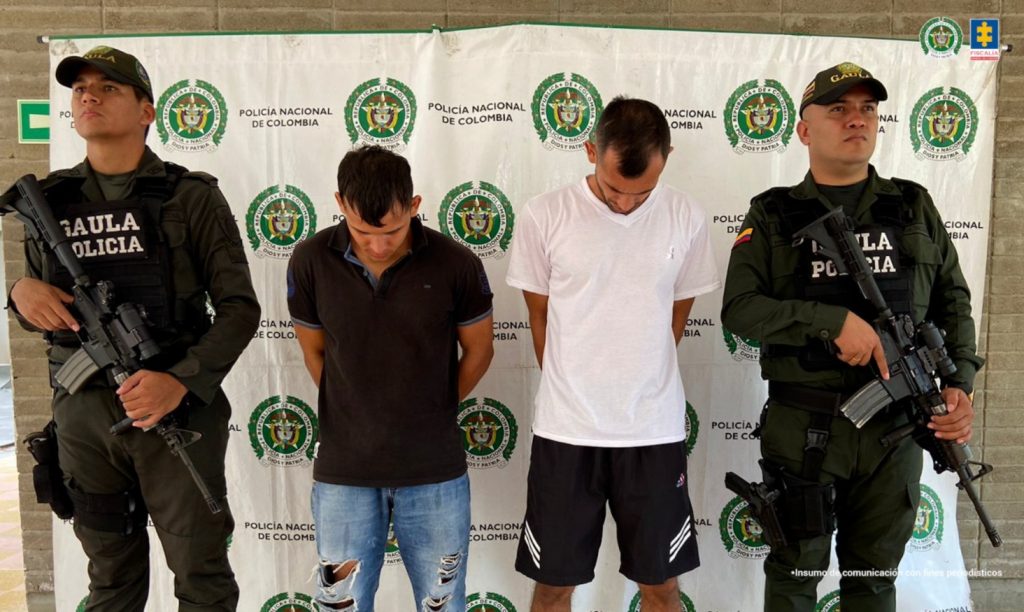 En la imagen hay dos personas detenidas bajo custodia de dos integrantes de la Policía Gaula. Detrás suyo un backing institucional.