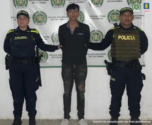 En la imagen se ve una persona detenida bajo custodia de dos integrantes de la Policía Nacional.