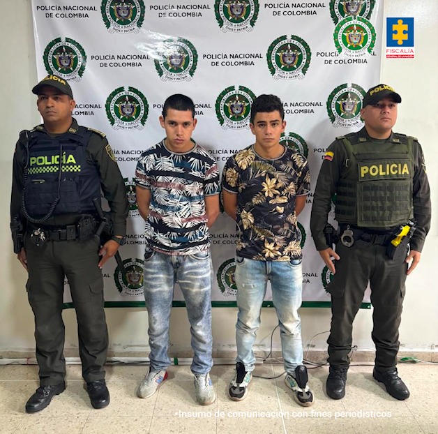 en la imagen se ven dos hombres detenidos bajo custodia de la Policía Nacional. Detrás suyo un backing institucional.
