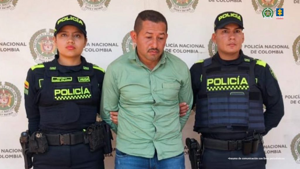 en la imagen se ve un hombre detenido bajo custodia de dos integrantes de la Policía Nacional.