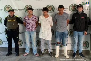 en la imagen se ven tres hombres detenidos bajo custodia de un investigador del CTI y un integrante de la Policía Nacional. Detrás suyo, un backing institucional.