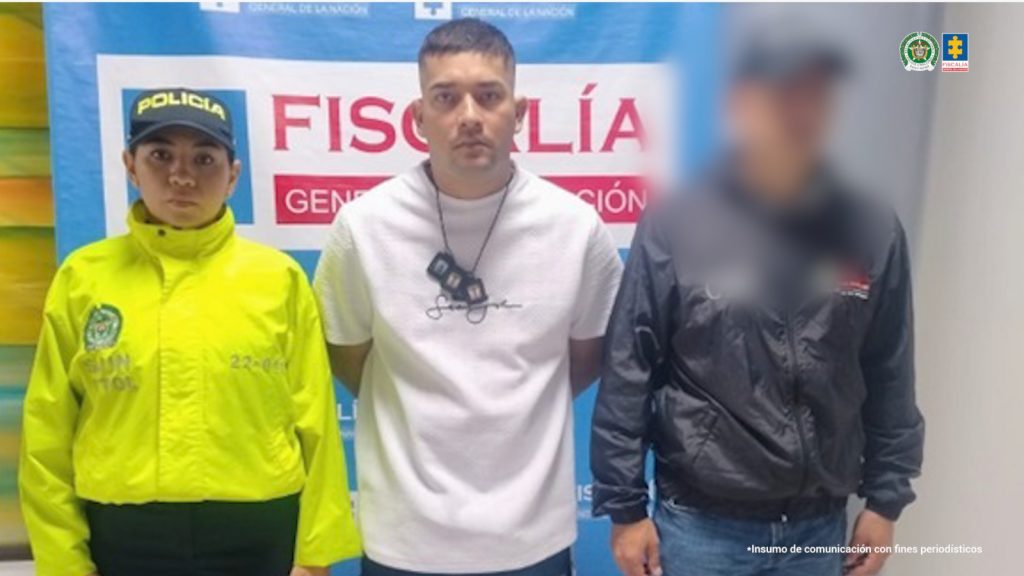 en la imagen se ve un hombre detenido bajo custodia de un integrante del CTI y la Policía Nacional. Detrás suyo, un backing institucional.