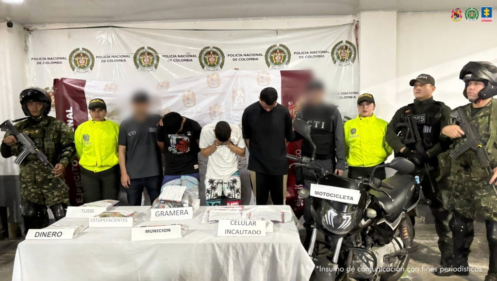 En la imagen se ven detenidas tres personas detenidas bajo custodia de servidores del CTI, Policía y Ejército. Delante de ellos una mesa con elementos incautados, detrás un backing institucional.