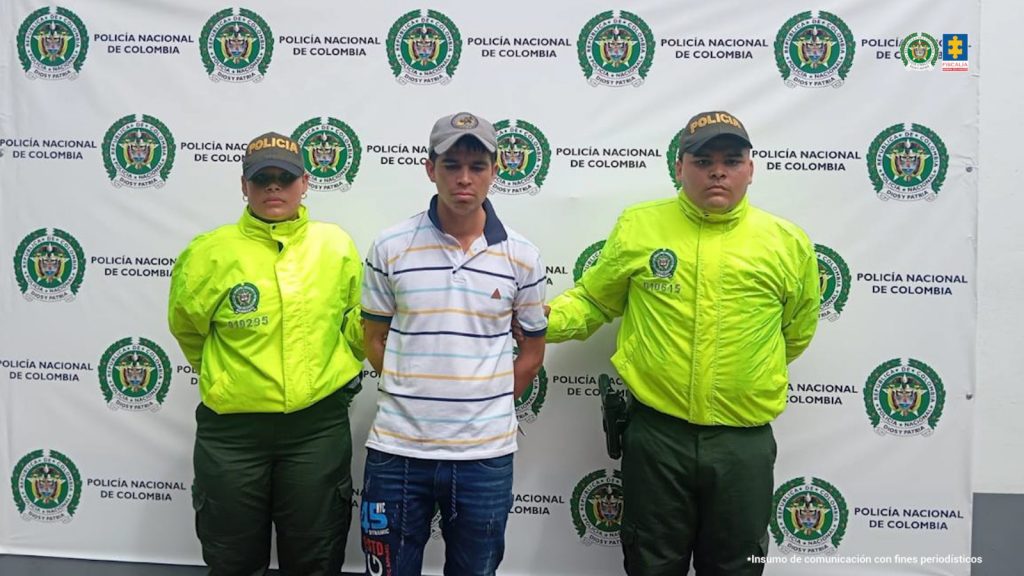 en la imagen se ve un hombre detenido bajo custodia de dos integrantes de la Policía Nacional.