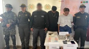 En la imagen se ve una pareja detenida bajo custodia de investigadores del CTI, integrantes del Ejército y la Policía Nacional. Detrás un backing institucional, adelante una mesa con elementos incautados.