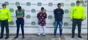 En la imagen se ven tres personas detenidas bajo custodia de la Policía Nacional. Detrás suyo un backing institucional.