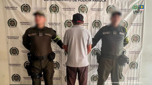  Se observa al capturado de espaldas junto a dos uniformados de la Policía Nacional. Detrás de ellos el banner que identifica a la Policía Nacional.