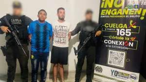 Se visualiza a los capturados junto a dos uniformados del Gaula de la Policía Nacional. Detrás de ellos el banner que identifica a la Policía Nacional