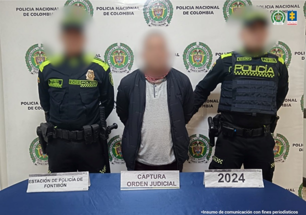 Se visualiza al capturado junto a dos uniformados de la Policía Nacional. Detrás de ellos el banner que identifica a la Policía Nacional.
