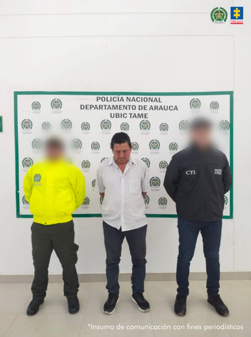 Se visualiza al capturado junto a un uniformado de la Policía Nacional y un investigador del CTI de la Fiscalía. Detrás de ellos el banner que identifica a la Policía Nacional.