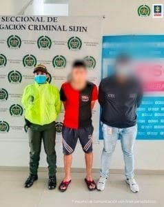 Se visualiza al capturado junto a un investigador del CTI y un uniformado de la Policía Nacional. Detrás de ellos los banners que identifican a la Policía Nacional y a la Fiscalía General de la Nación.