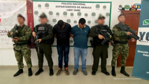Se visualiza a dos capturados junto a un uniformado del Gaula Militar y de la Policía Nacional. Detrás de ellos el banner de la Policía Nacional.