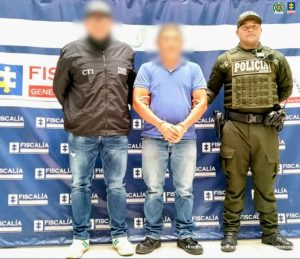 En la fotografía aparece el detenido junto a un funcionario del CTI y un uniformado de la Policía. En la parte superior está un banner de la Fiscalía General