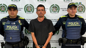 Se visualiza al capturado junto a dos uniformados de la Policía Nacional. Detrás de ellos el banner que identifica a la Policía Nacional.
