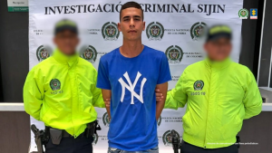 Se visualiza al capturado junto a dos uniformados de la Policía Nacional. Detrás de ellos el banner que identifica a la Policía Nacional.