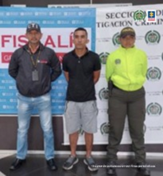 En la fotografía aparece el capturado junto a un investigador del CTI y una uniformada de la Policía Nacional. En la parte posterior se observan los banners que identifican a la Fiscalía General de la Nación y a la Policía Nacional