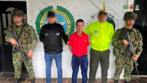 Se observa al capturado, junto a un investigador del CTI y uniformados de la Policía y Ejército Nacional. Detrás de ellos los banners que identifican a la Policía y Ejército Nacional.