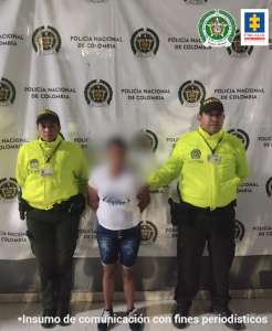 Fotograía en la que aparece la señalada agresora acompañada de dos uniformados de la Policía Nacional. La mujer viste camiseta blanca, pantaloneta de jean y tenis negros. Le fue cubierta la cara para evitar la identificación de la víctima que es menor de edad.