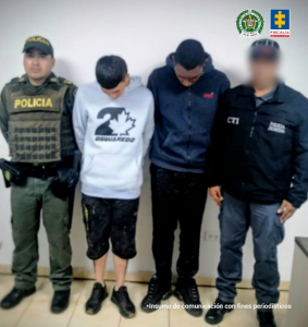 En la imagen aparecen dos hombres con la cabeza inclinada hacia abajo, custodiados por autoridades.A la izquierda está un uniformado de la Policía Nacional de Colombia, con chaleco antibalas que lleva la palabra POLICÍA en color amarillo. A la derecha, otro funcionario viste chaqueta negra con las siglas CTI (Cuerpo Técnico de Investigación de la Fiscalía General de la Nación). En la parte superior derecha se observan los logotipos de la Policía Nacional de Colombia y de la Fiscalía General de la Nación. En la parte inferior, nuevamente aparece la frase: “Insumo de comunicación con fines periodísticos”, indicando que la foto hace parte de un comunicado oficial.