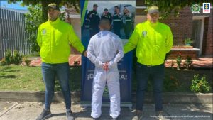 En la imagen se aprecia al capturado de espaldas junto a uniformados de la Policía Nacional. Detrás de ellos se observa un banner de la Policía Nacional