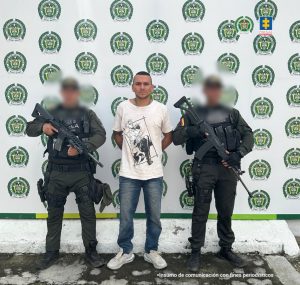 Se visualiza al capturado junto a dos uniformados del Gaula de la Policía Nacional. Detrás el banner que identifica a la Policía Nacional.