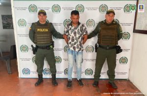 En la imagen se aprecia el capturado junto a dos uniformados d la Policía Nacional. En la parte posterior se visualiza el banner que identifica a la Policía Nacional.