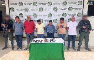 Se visualiza a los capturados junto a dos uniformados de la policía Nacional. Frente a ellos una mesa con los elementos incautados. Detrás de ellos el banner que identifica a la Policía Nacional.