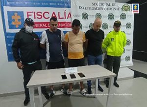En la gráfica aparecen tres de los capturados, junto a un investigador del Cuerpo Técnico de Investigación y de la Policía Nacional. En la parte posterior los banners que identifican a la Fiscalía General de la Nacional y a Seccional de Investigación Criminal de la Policía Nacional.