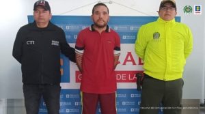  En la imagen se aprecia al capturado junto a un investigador del CTI y un uniformado de la Policía Nacional. Detrás de ellos se aprecia el banner que identifica a la Fiscalía General de la Nación. 