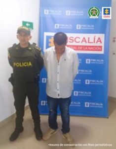En la imagen se observa el capturado junto a un uniformado de la Policía Nacional. En la parte posterior se encuentra el banner que identifica a la Fiscalía General de la Nación.